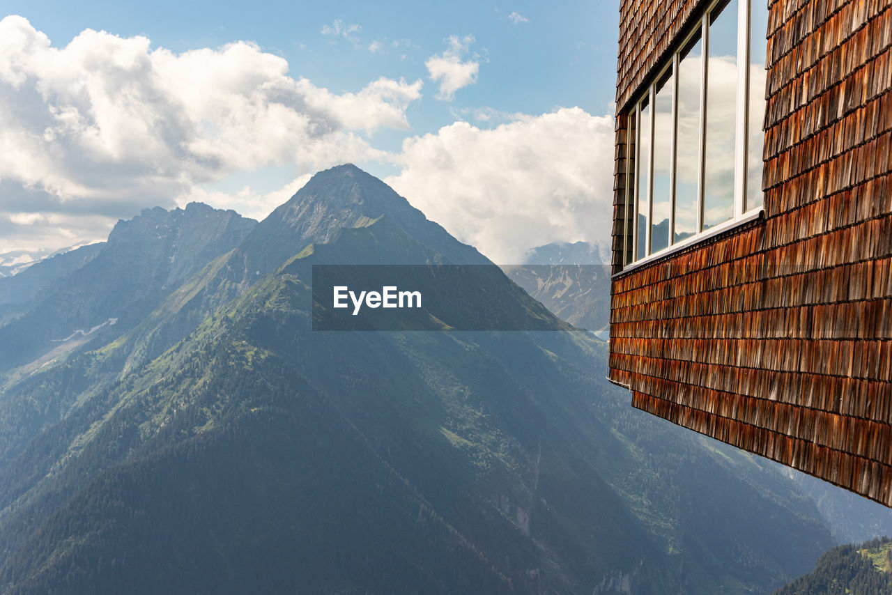 The wall of the building with windows is covered with wooden shingles and a view of the mountain