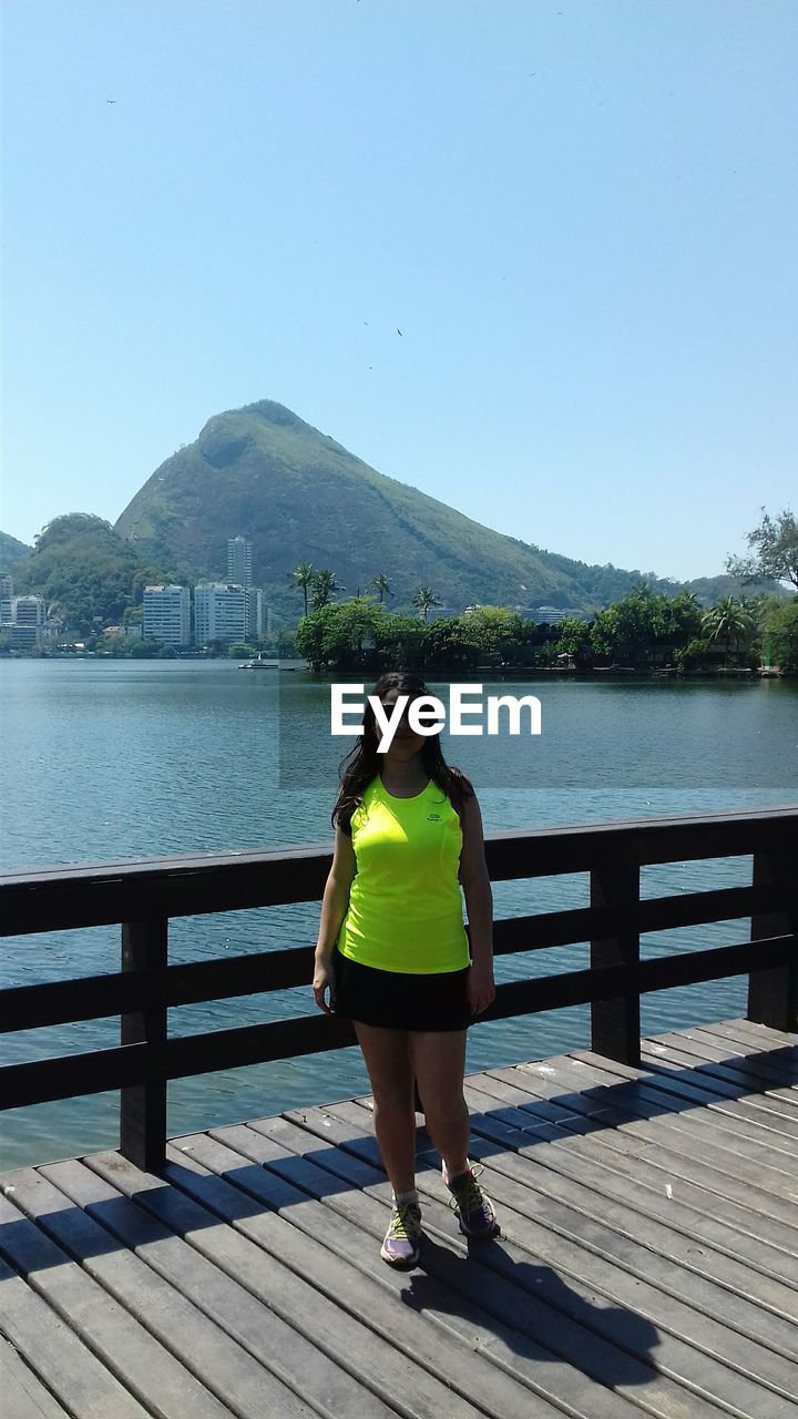 Portrait of woman standing on boardwalk against lake