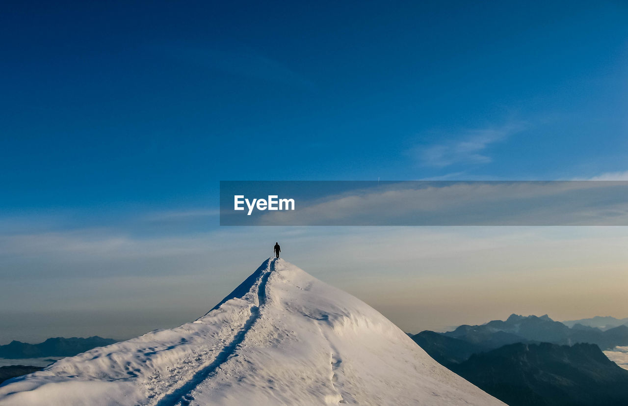 Person on peak of snowcapped mountains against sky