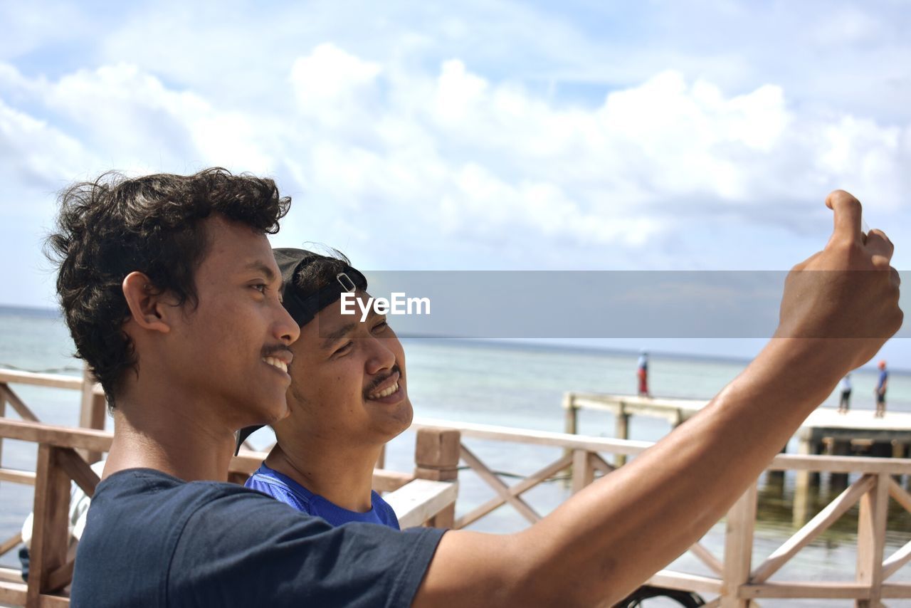 Friends taking selfie by sea against sky