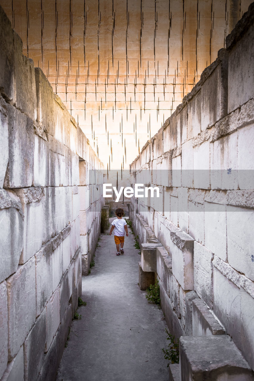 REAR VIEW OF PEOPLE WALKING ON ALLEY AMIDST WALL