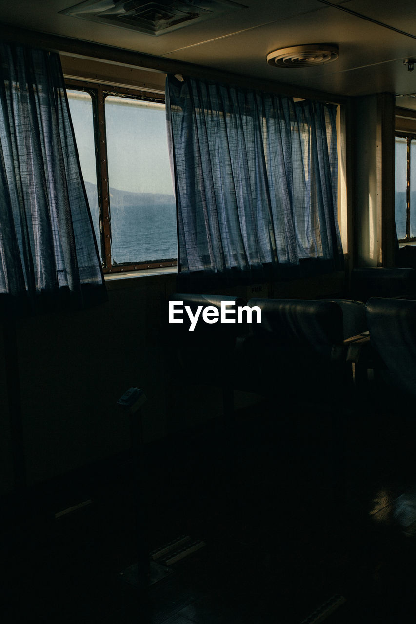 The passenger seats on the ferry boat, view through the window and curtains  behind which is sea.