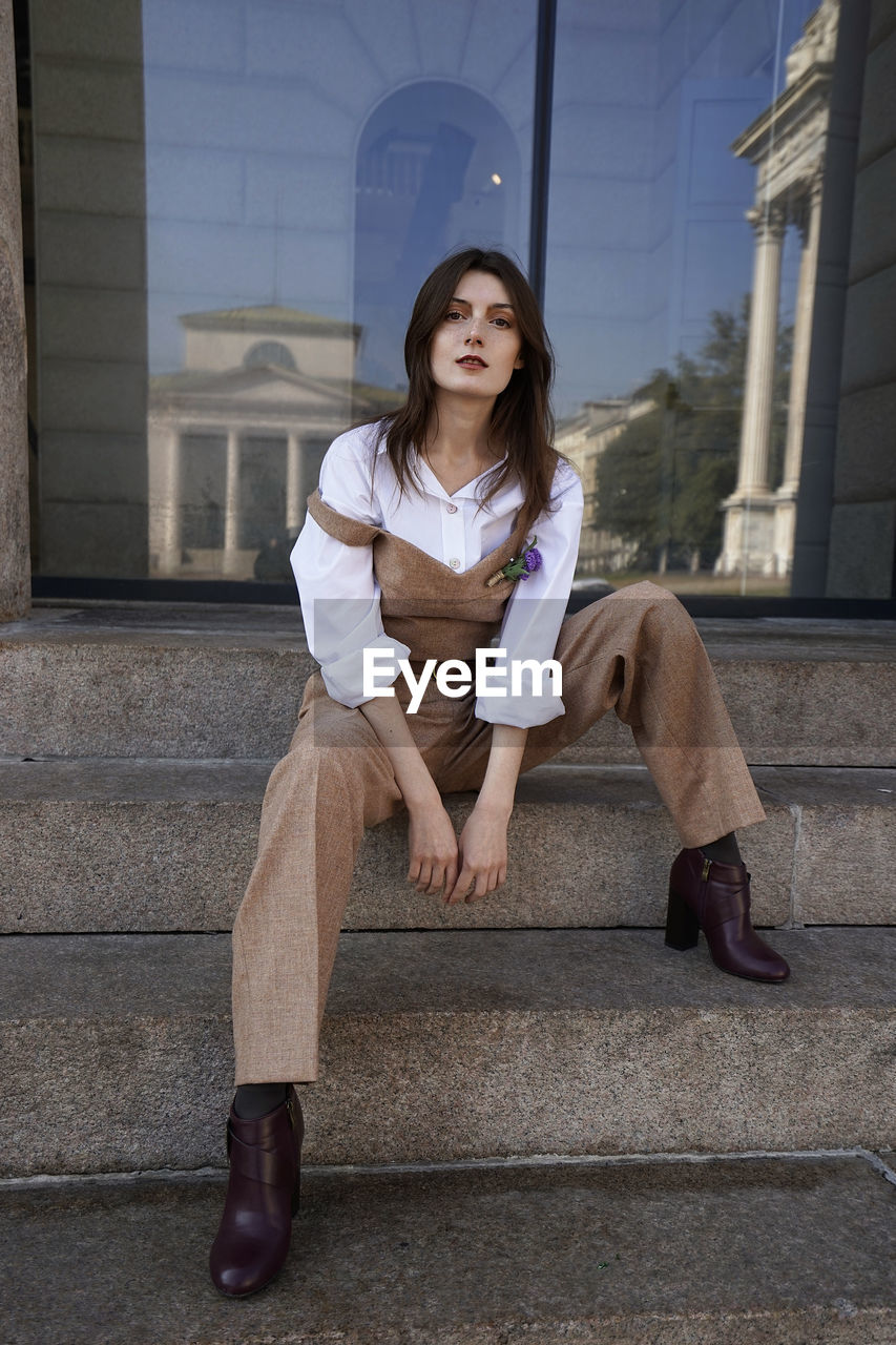 Full length portrait of young woman sitting on steps