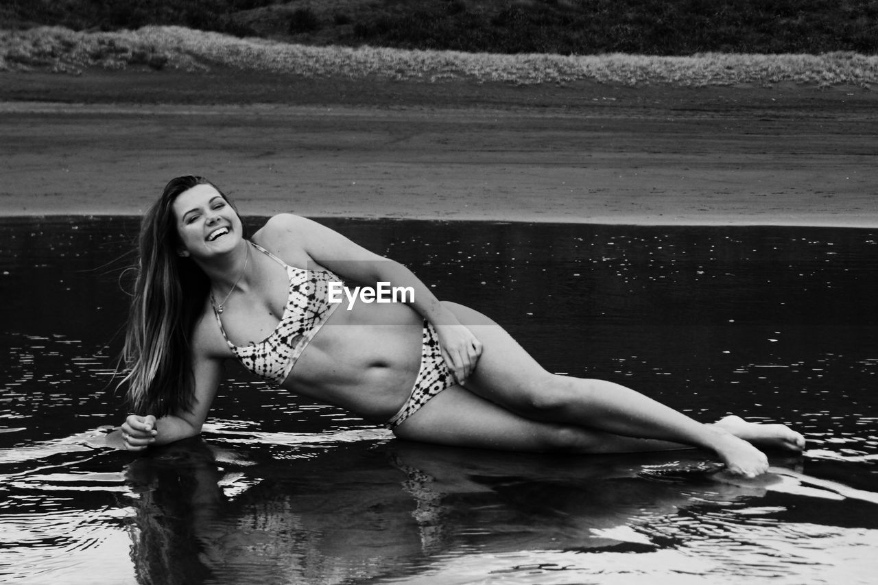 Happy woman in bikini lying on shore at beach