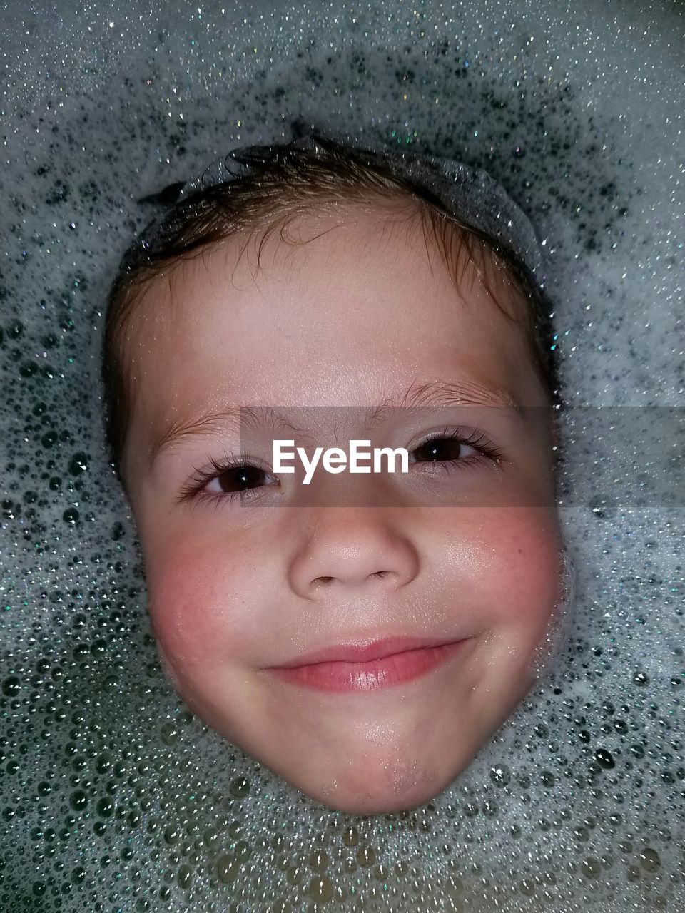 Directly above shot of boy smiling amidst soap sud in bathtub