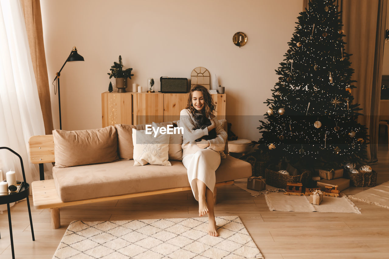 Smiling happy girl hugging her pet cat while sitting by a decorated christmas tree in a cozy living