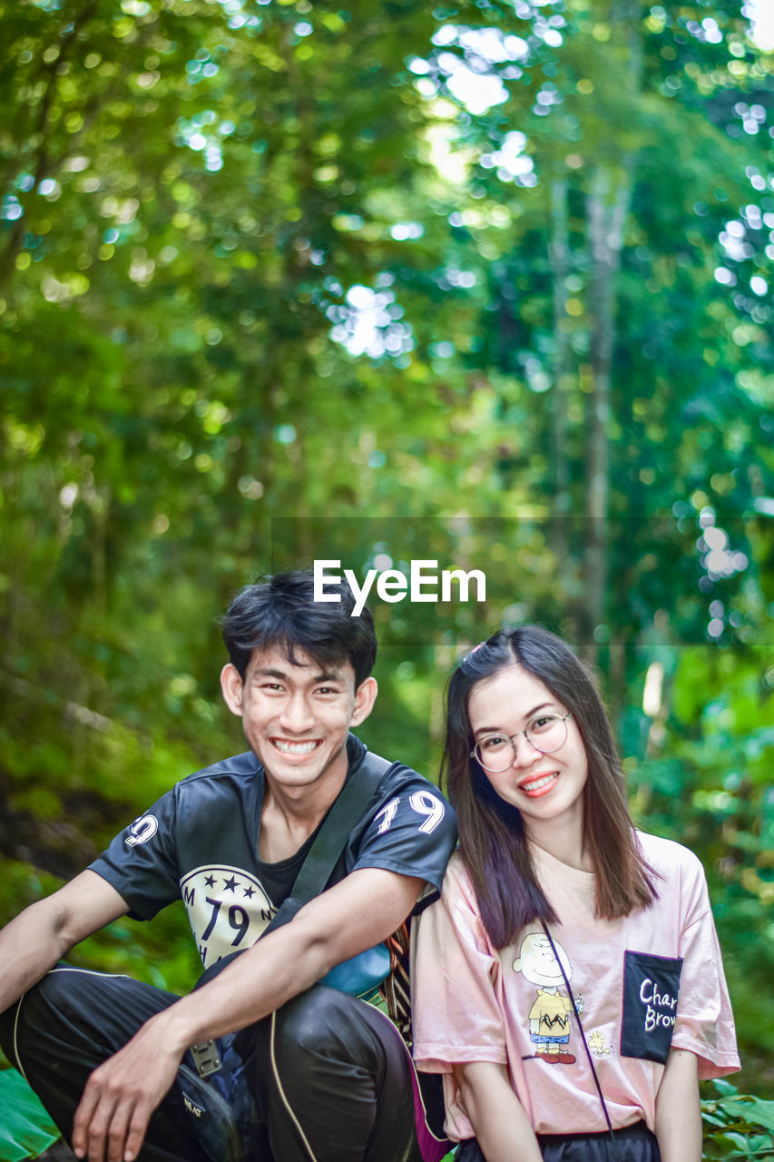 Portrait of smiling young couple sitting against trees