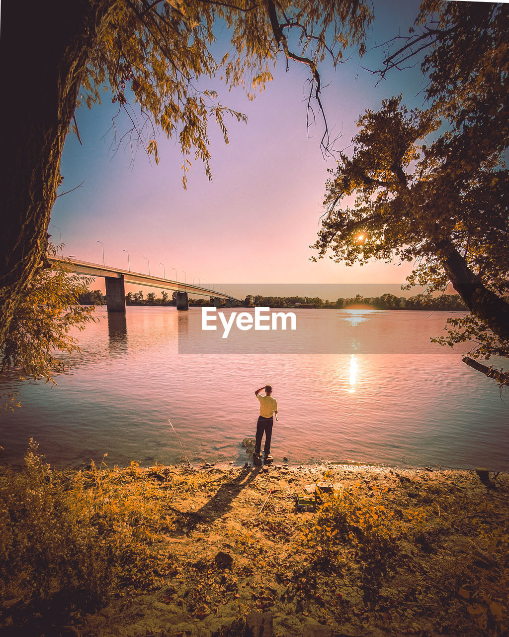 Rear view of man standing by river during sunset