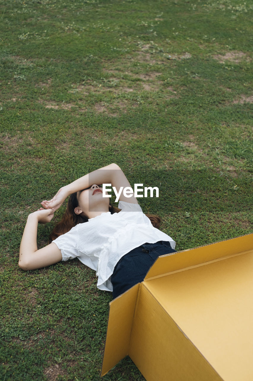 Woman lying on grass in cardboard box