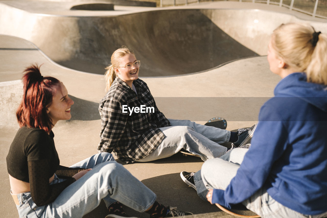 Teenage girls with skateboards sitting in skatepark