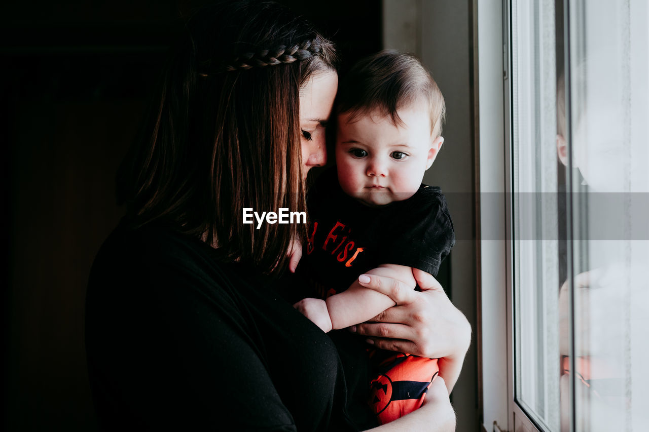 Mother and daughter embracing while standing by window at home