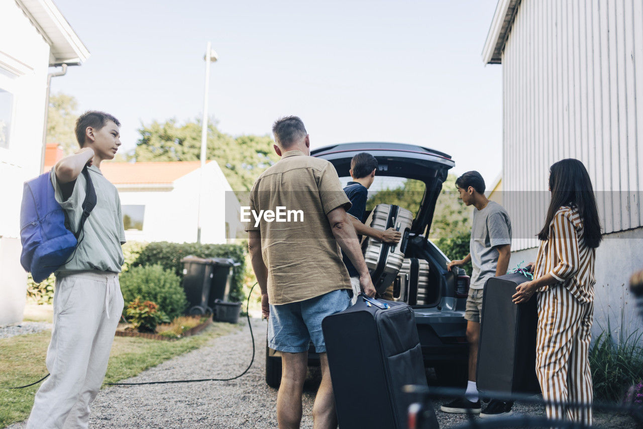 Family loading luggage in car trunk for vacations while standing in back yard