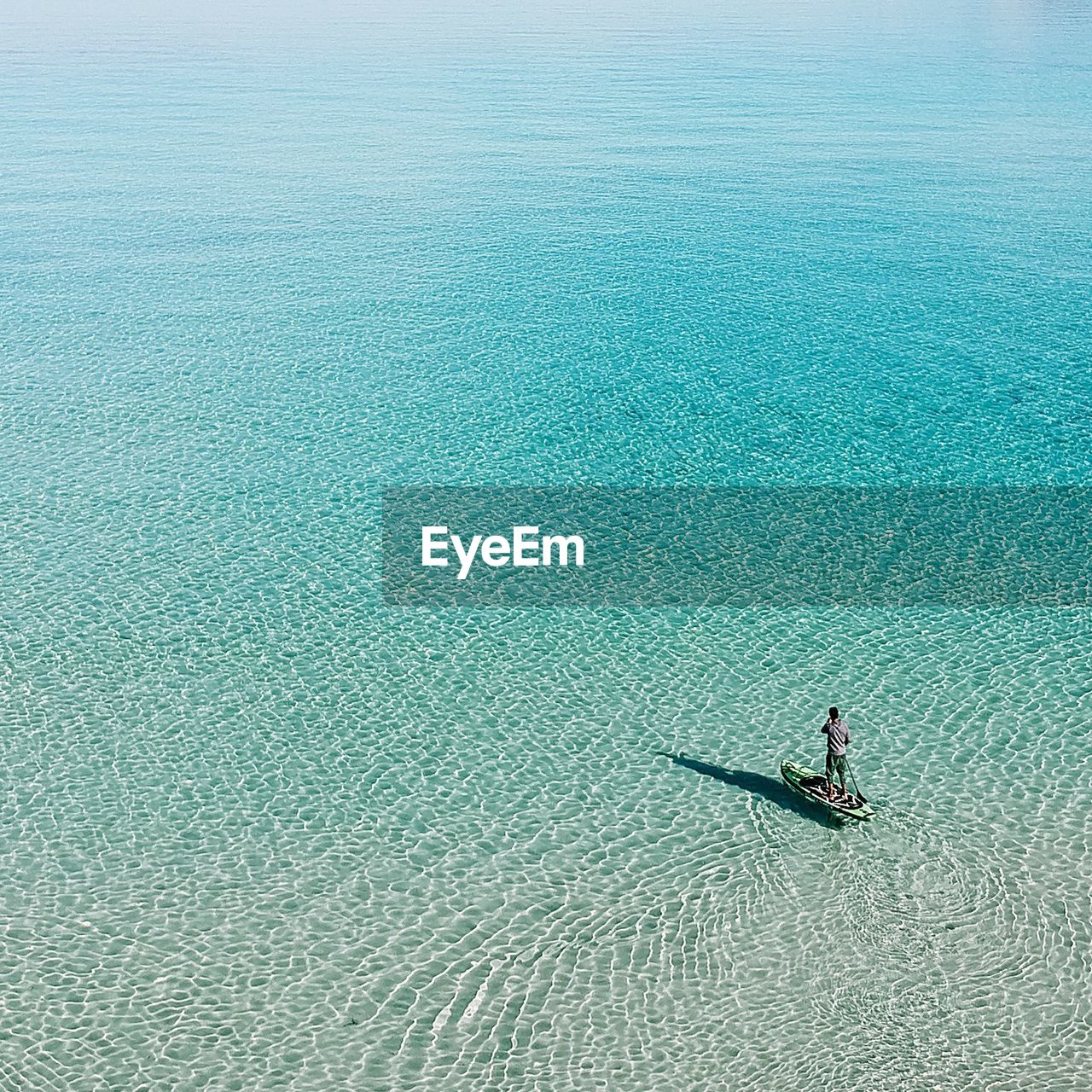 High angle view of mature man paddleboarding on sea during sunny day