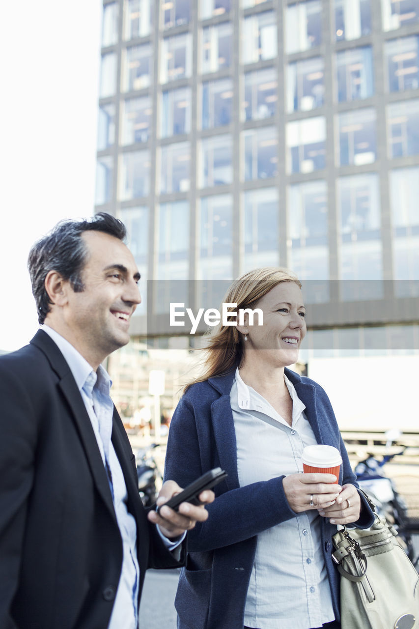 Happy businesspeople looking away while standing outside office building