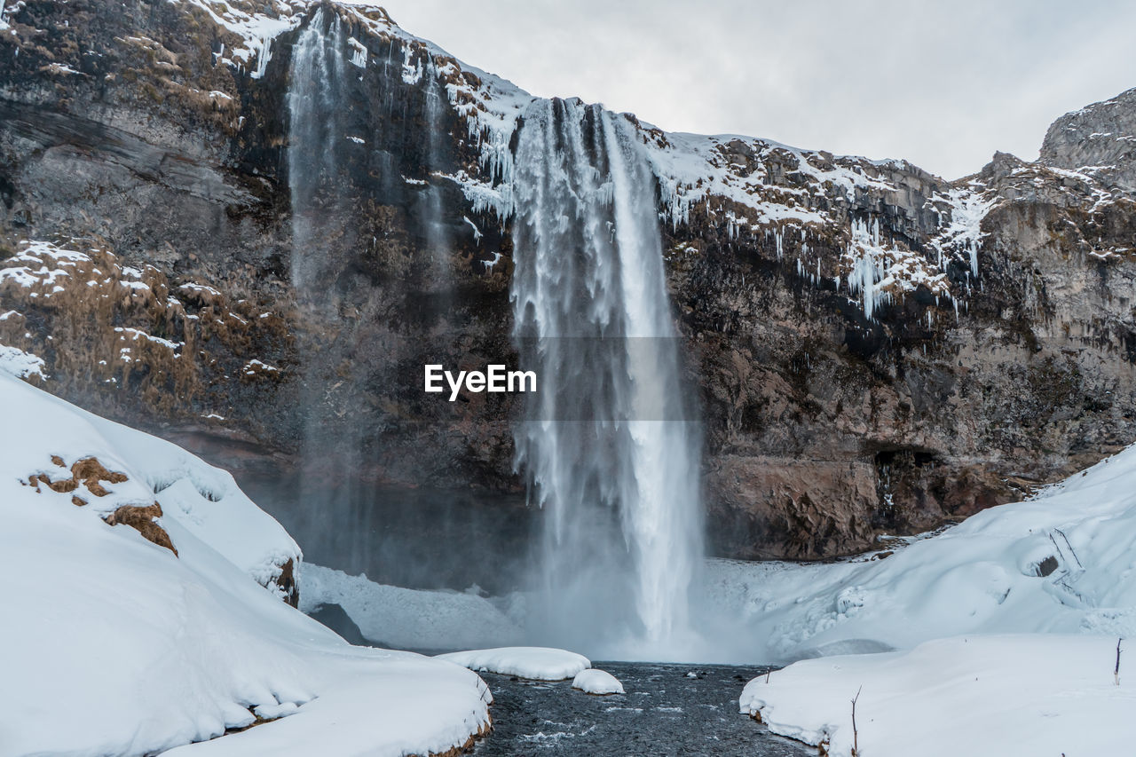 SCENIC VIEW OF WATERFALL AGAINST SNOWCAPPED MOUNTAIN