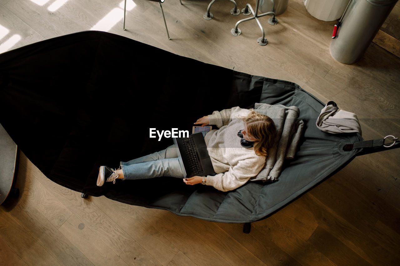 High angle view of businesswoman with laptop sitting on hammock in office