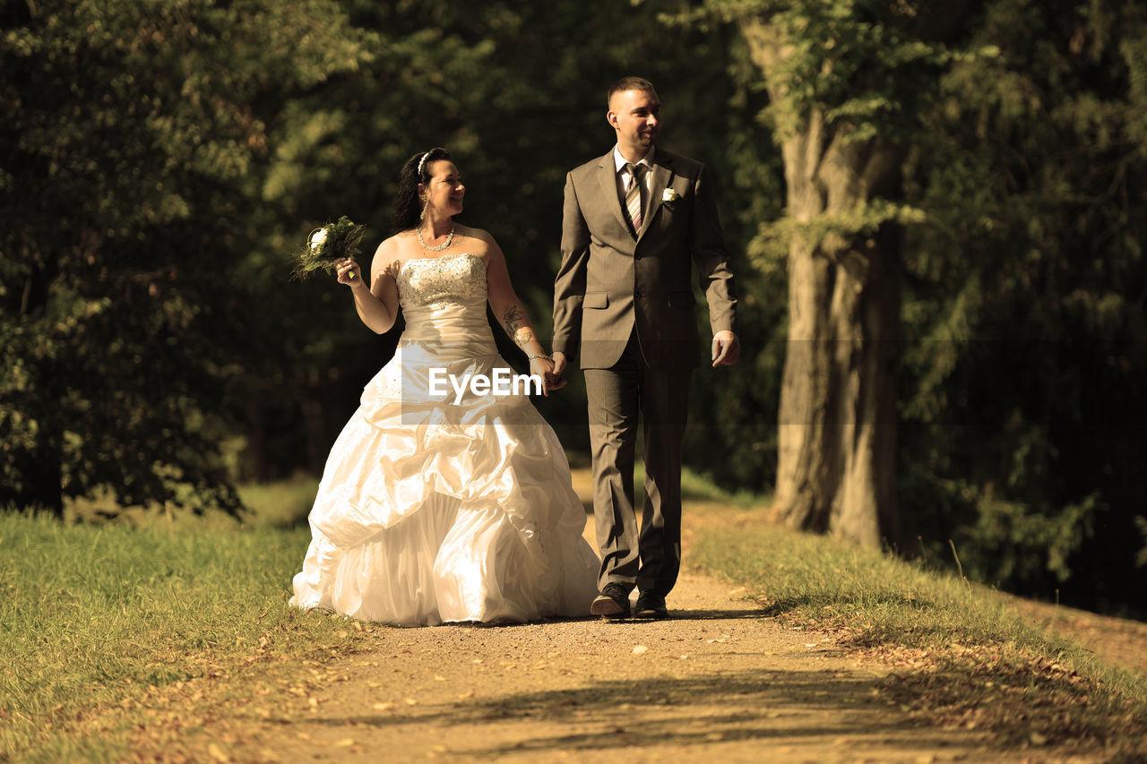 Full length of newly wed couple walking on field in park