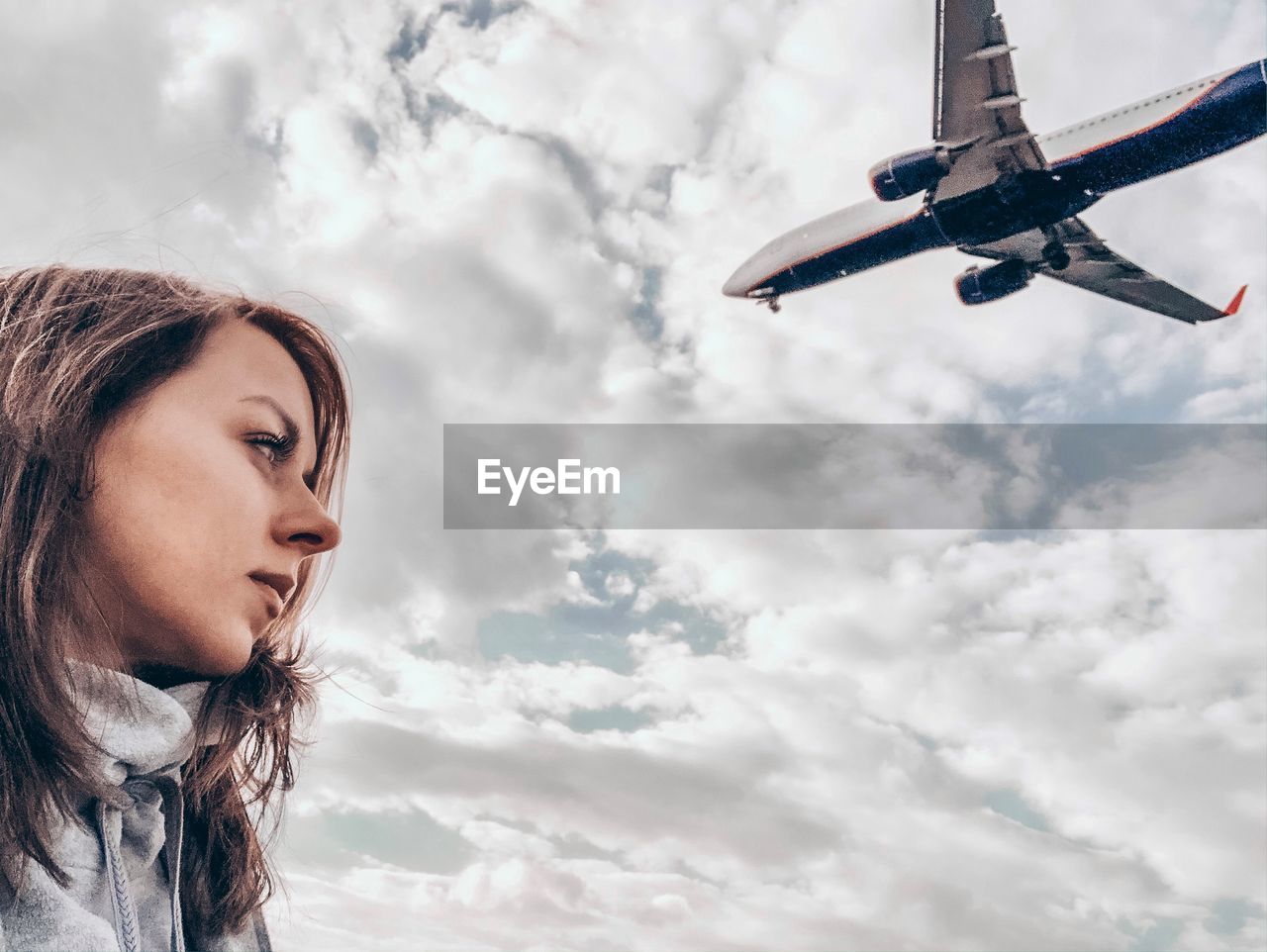 Low angle view of woman standing against plane flying in sky