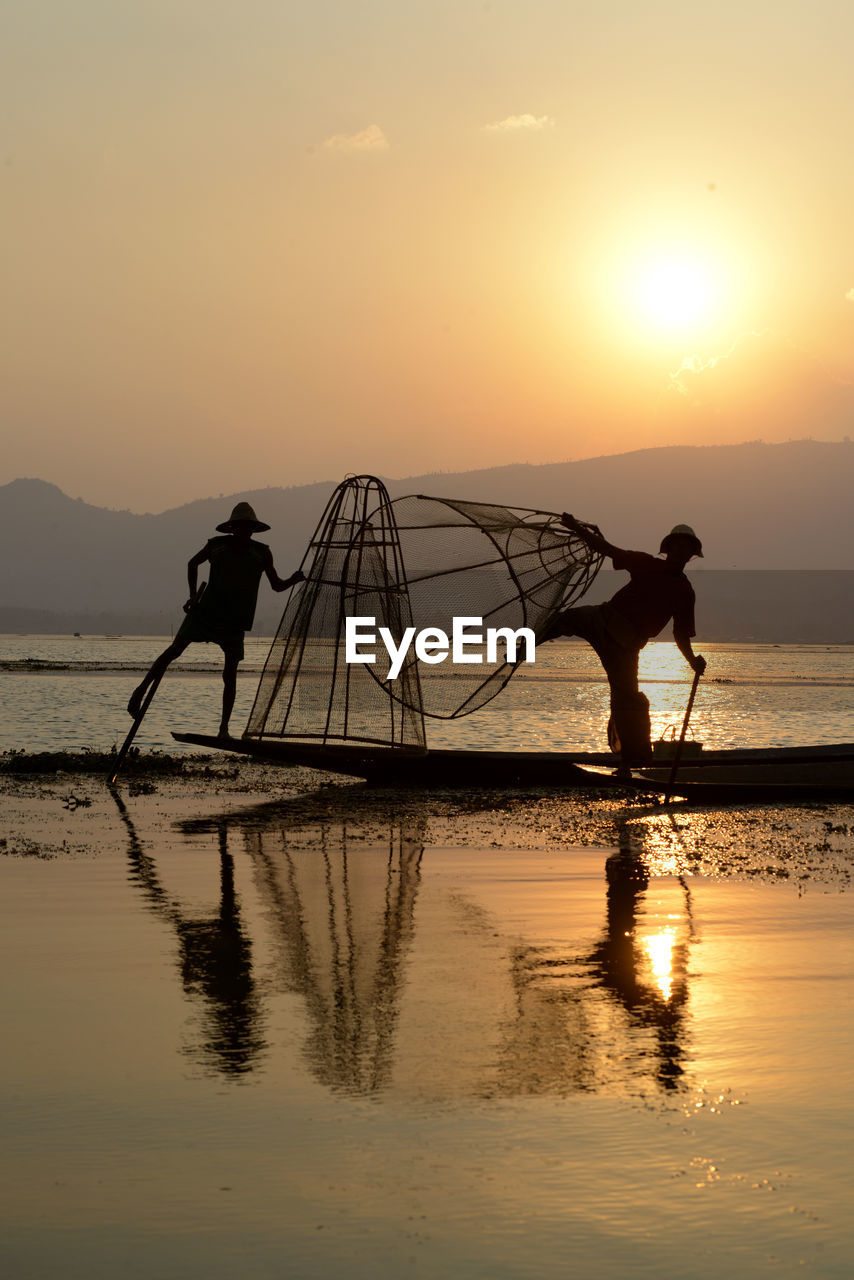 Silhouette men fishing in lake at sunset