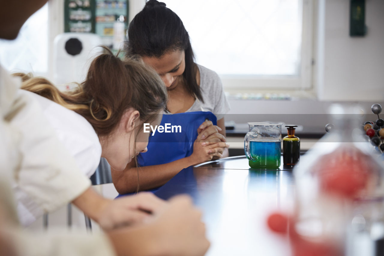 Female students looking at liquid solution in beaker in chemistry laboratory