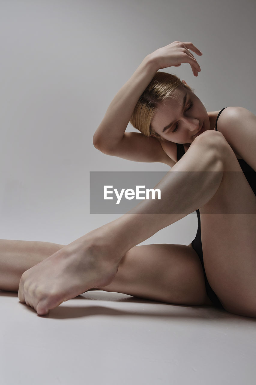 A ballerina  sexually sits on the floor demonstrating an eversion and stretching of the foot