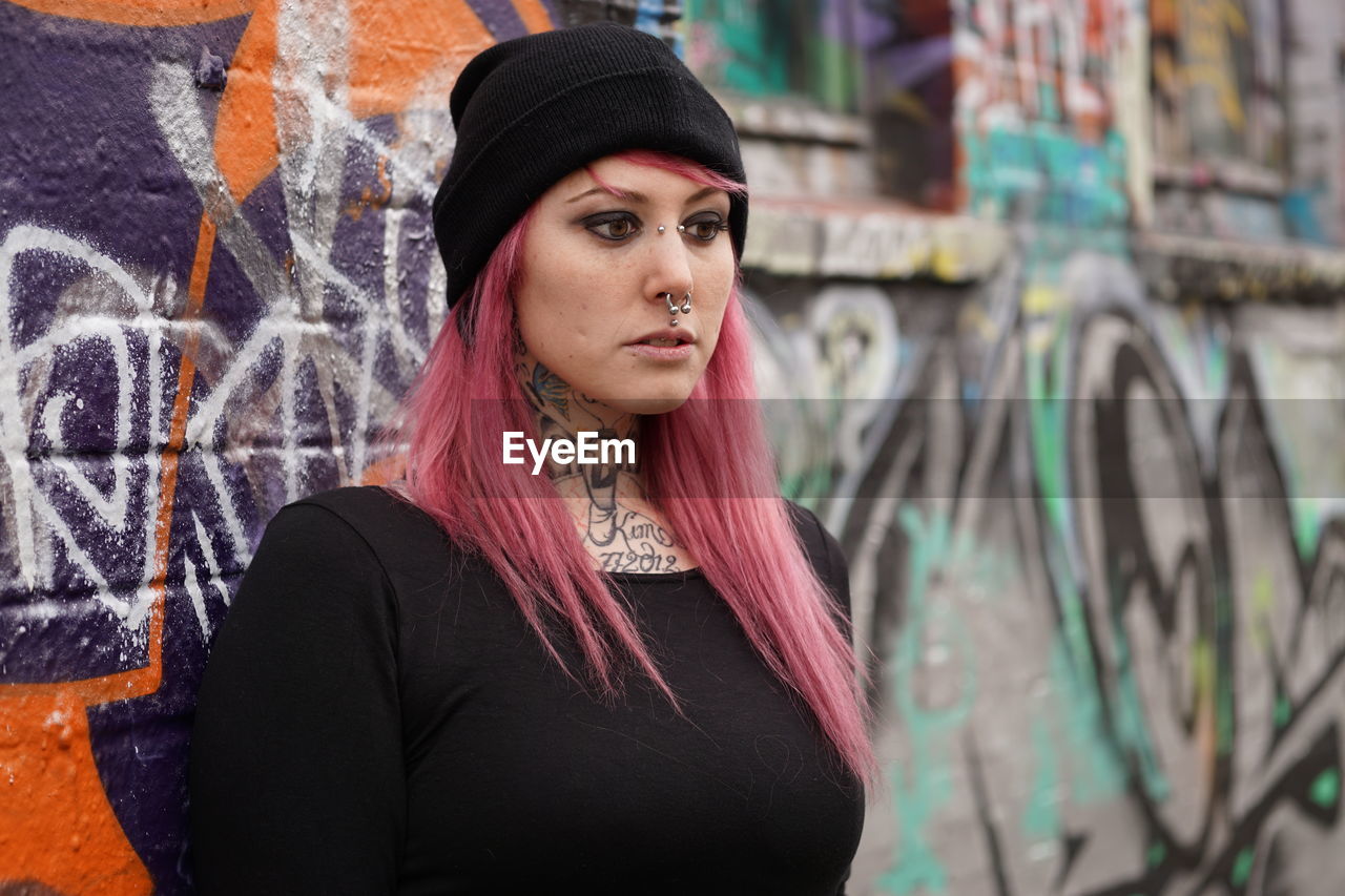 Young woman with pink hair standing against graffiti wall