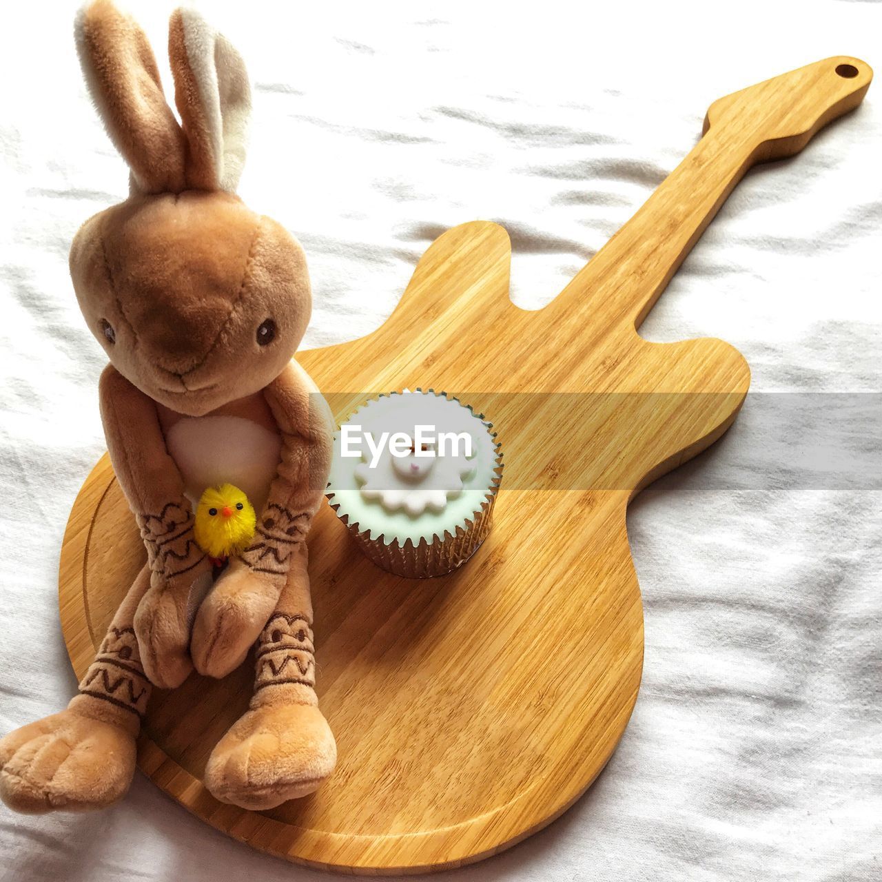 Easter bunny and easter chick next to  easter  iced cupcake on a wooden guitar shaped board 