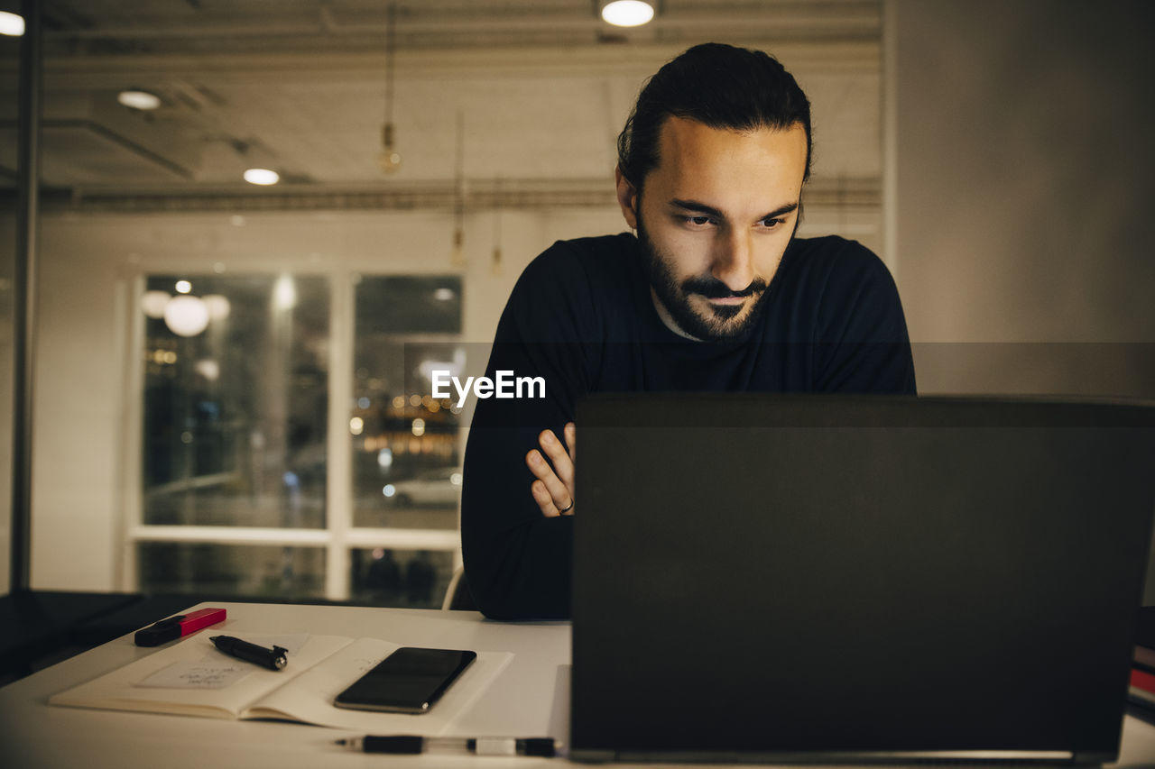 Confident businessman looking at laptop while working late in office