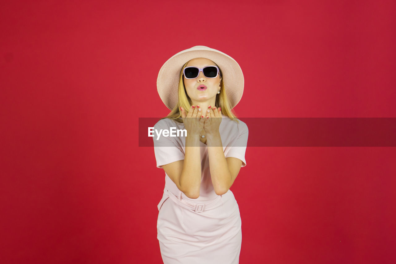 YOUNG WOMAN WEARING SUNGLASSES AGAINST RED BACKGROUND