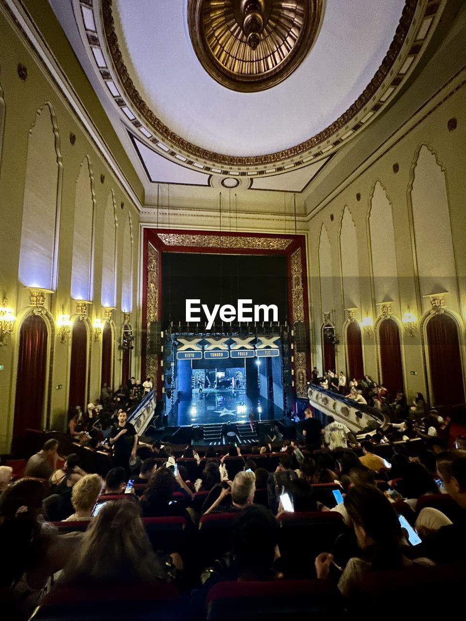 group of people, crowd, architecture, indoors, auditorium, arts culture and entertainment, large group of people, theatre, ballroom, stage, built structure, function hall, seat, lighting equipment, audience, convention, music, building, illuminated, person