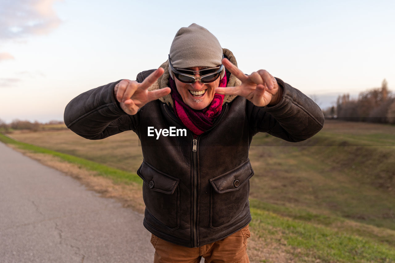 Middle aged man wearing winter clothes have fun and making victory sign with hands outdoors