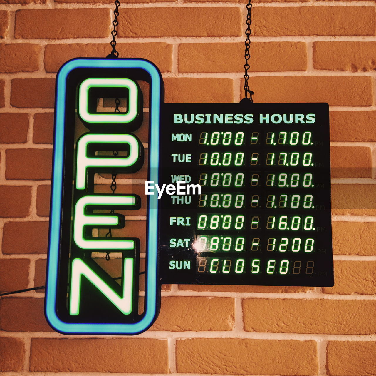 Low angle view of illuminated open sign by brick wall