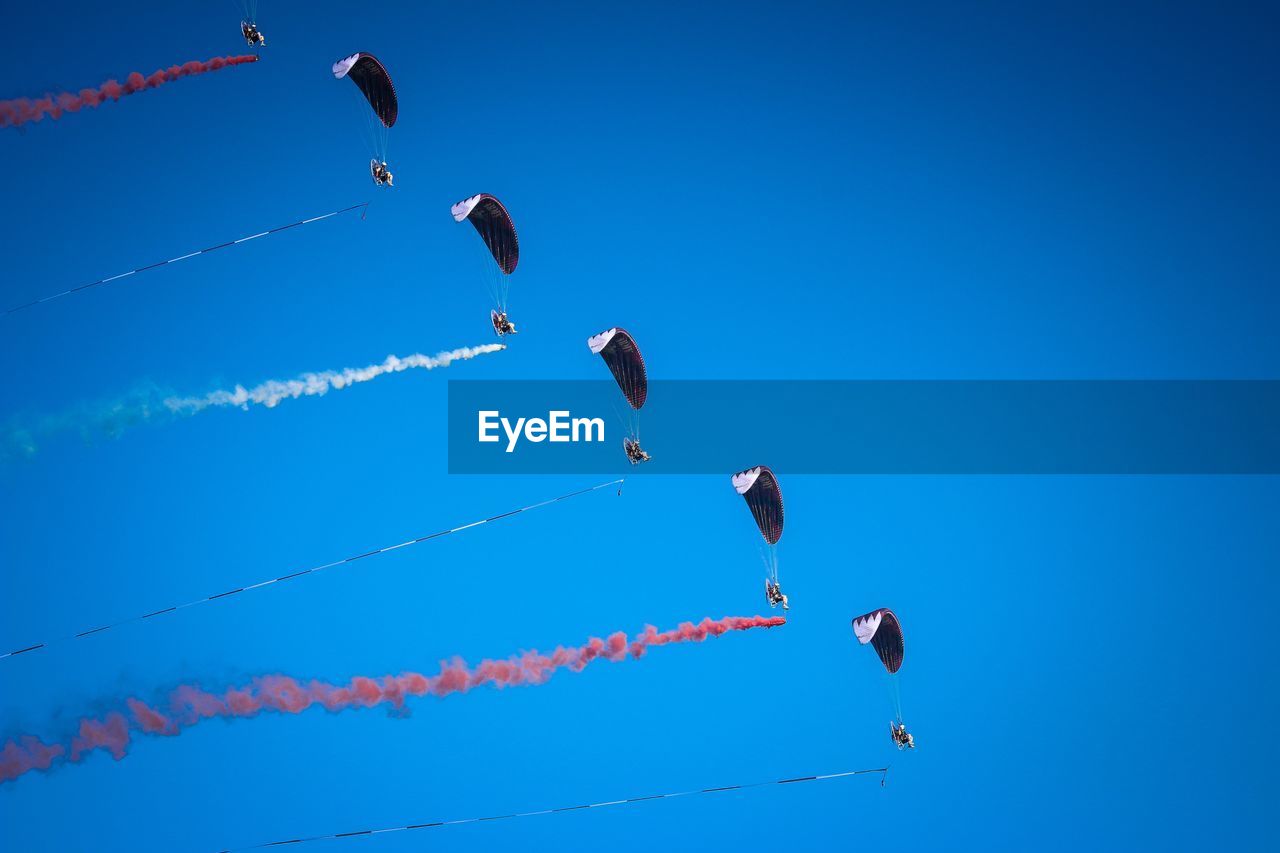 Low angle view of people paragliding against clear blue sky during sunny day