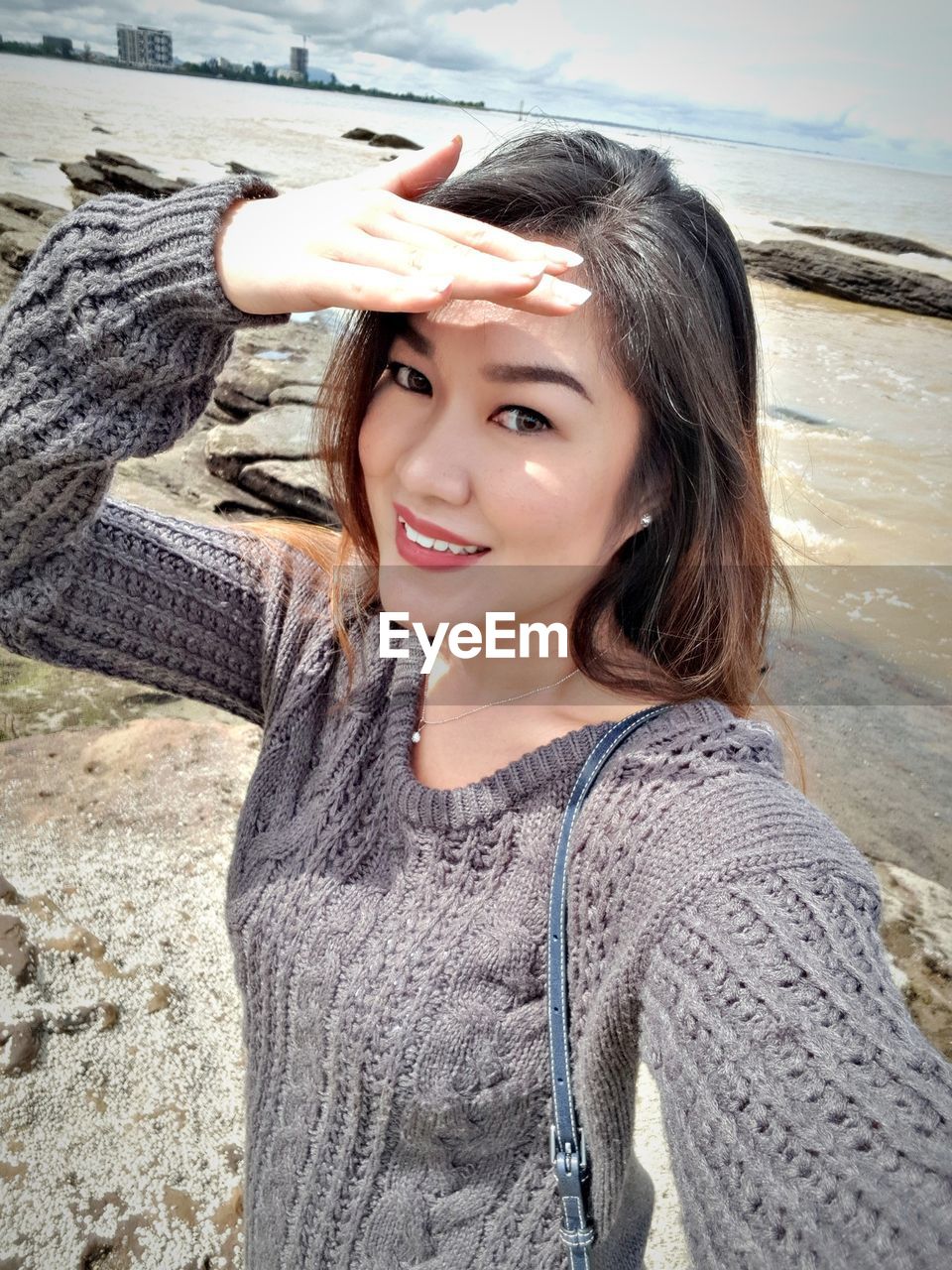 Portrait of smiling woman shielding eyes at beach