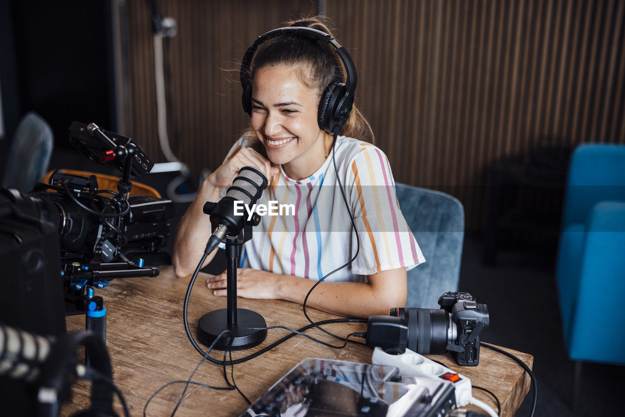 Happy influencer wearing headphones talking into microphone and vlogging in studio