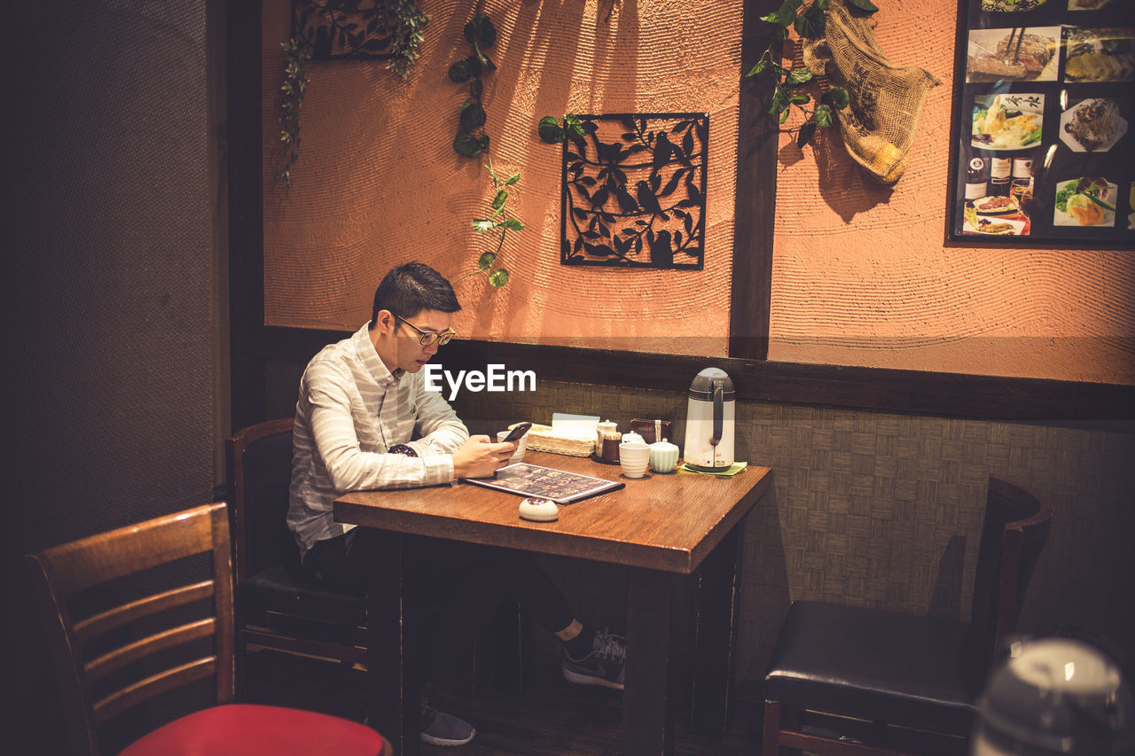 Man using mobile phone while sitting in restaurant at night