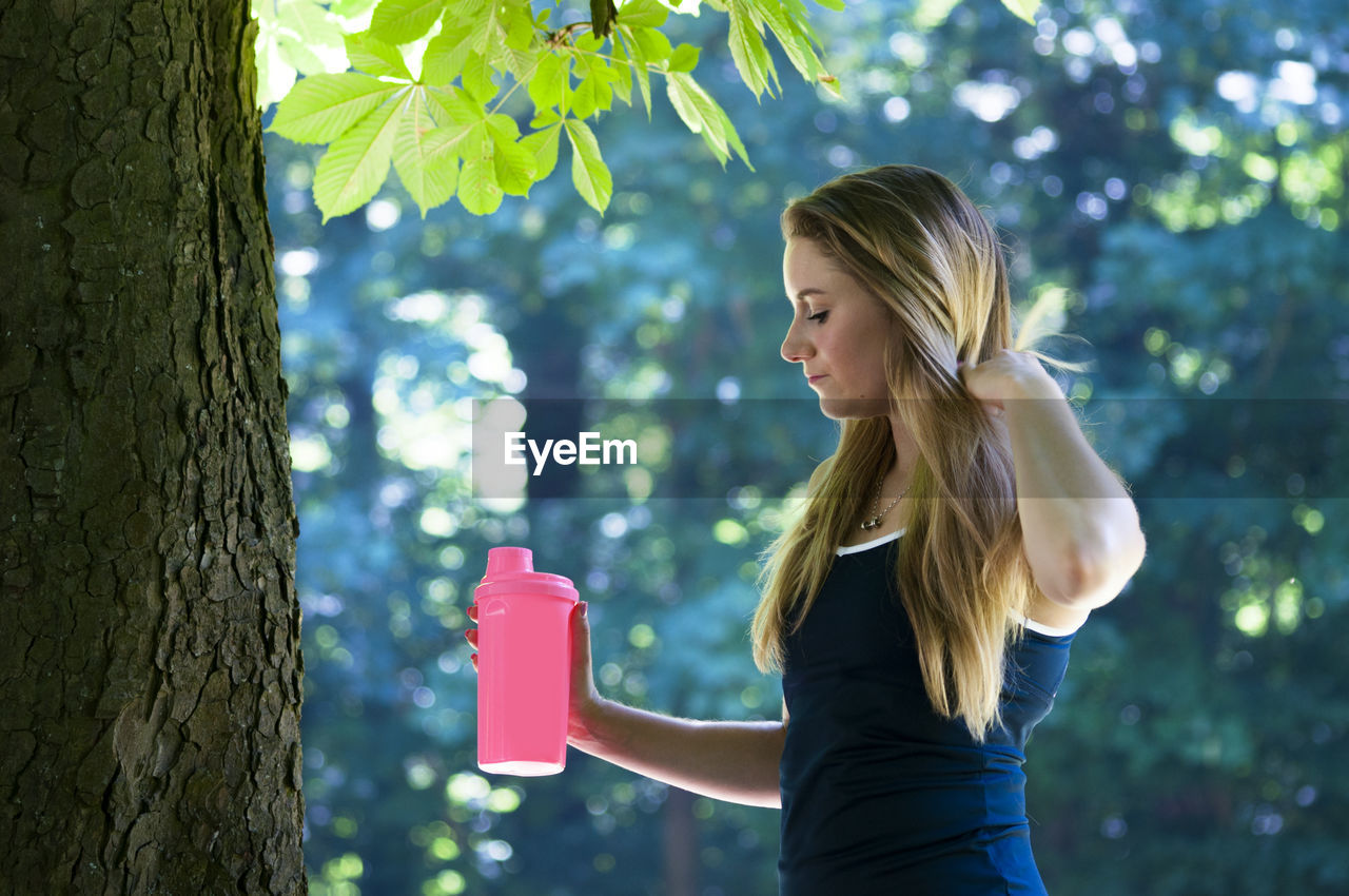 Woman holding water bottle against tree