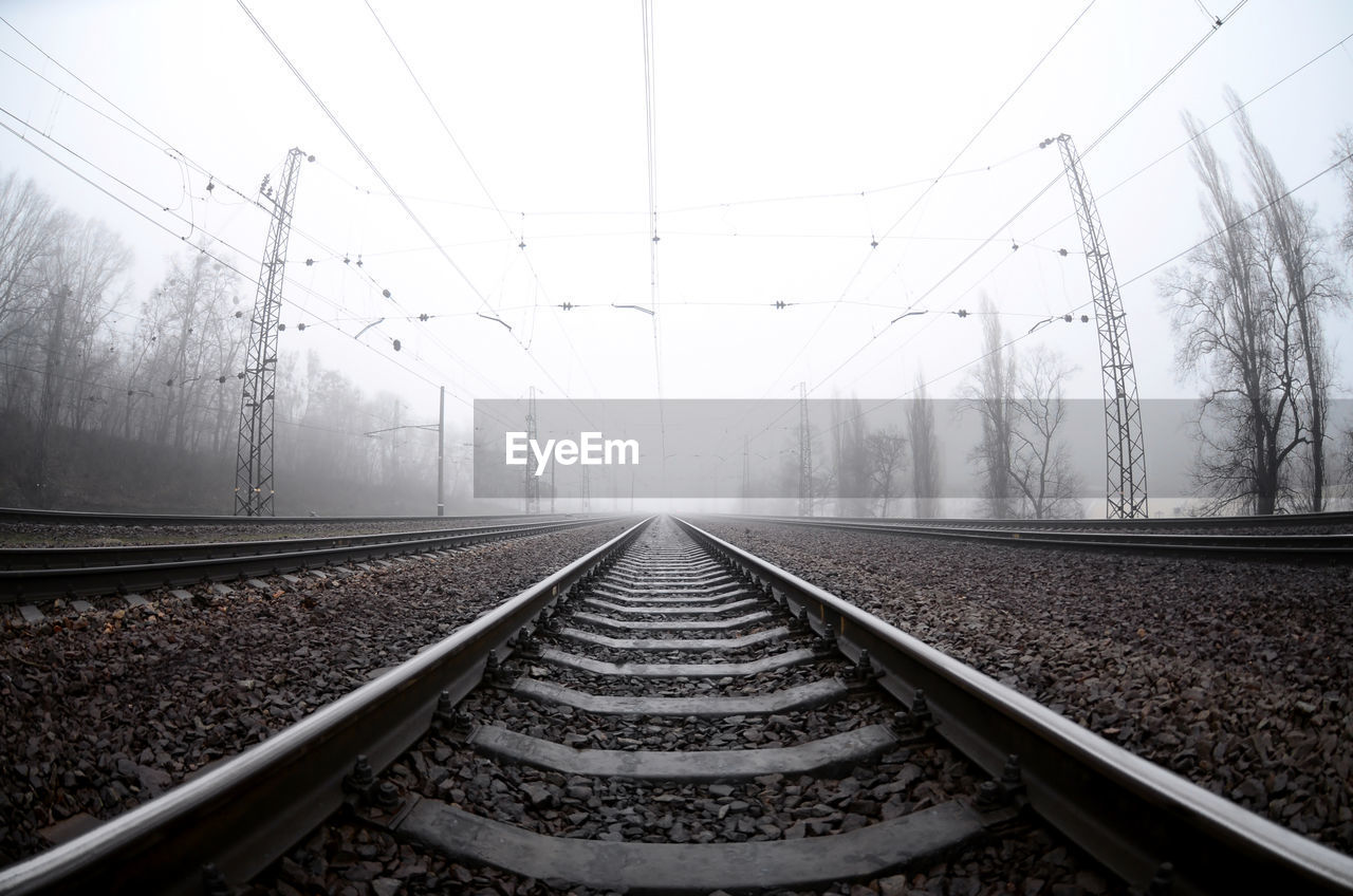 Diminishing perspective of railroad track against sky during foggy weather