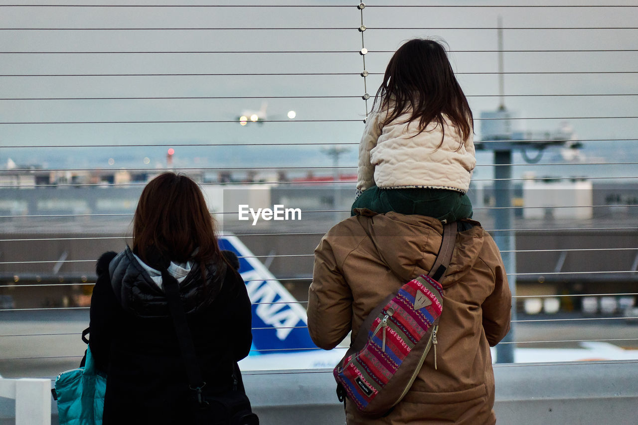 REAR VIEW OF WOMAN WALKING IN FRONT OF CITY