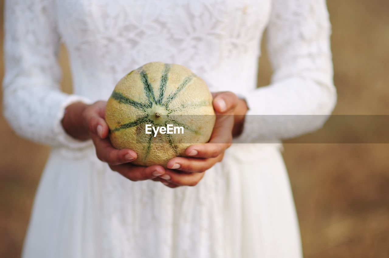 Midsection of bride holding melon outdoors