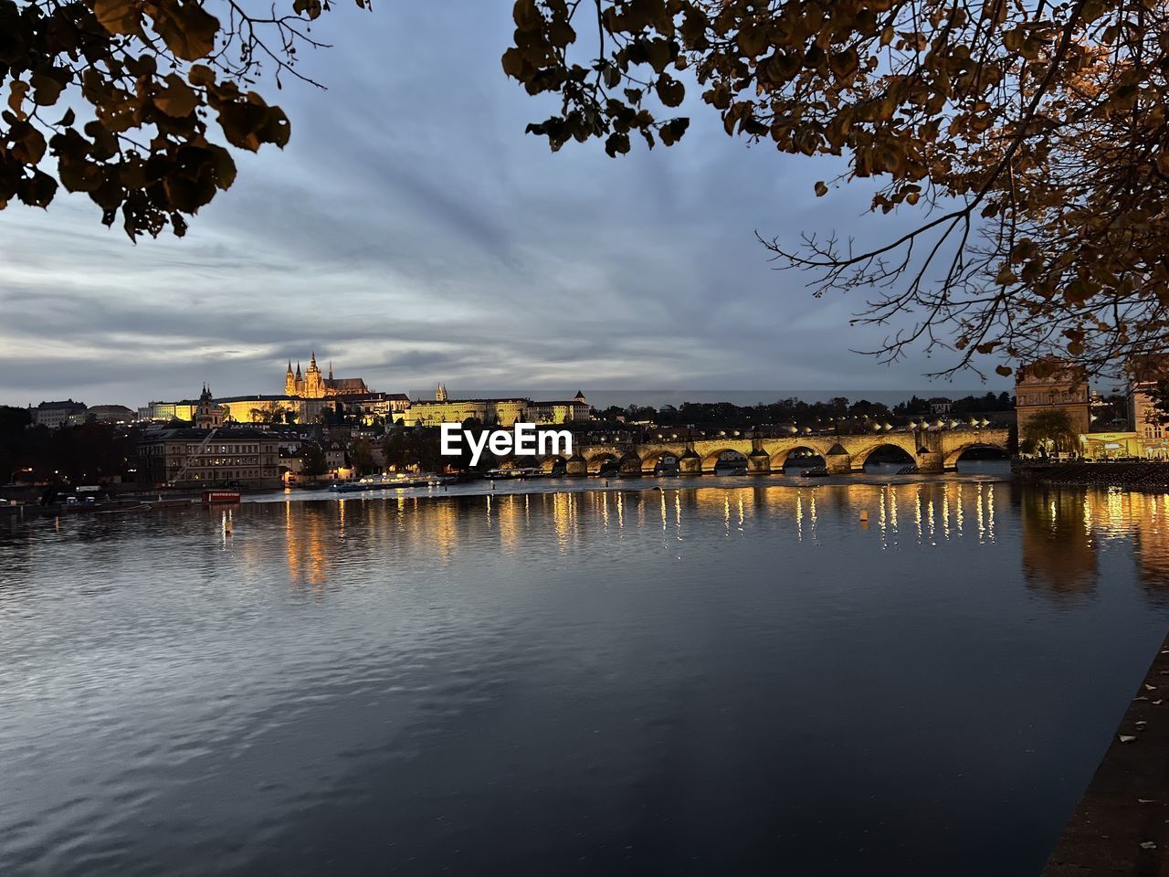 BUILDINGS BY RIVER AGAINST SKY AT DUSK