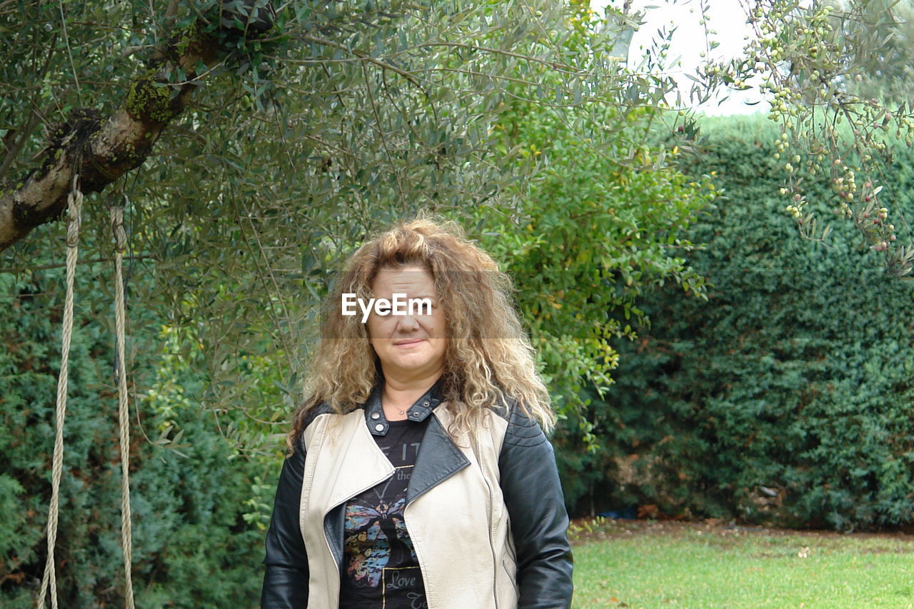 Portrait of smiling mature woman standing against plants in park