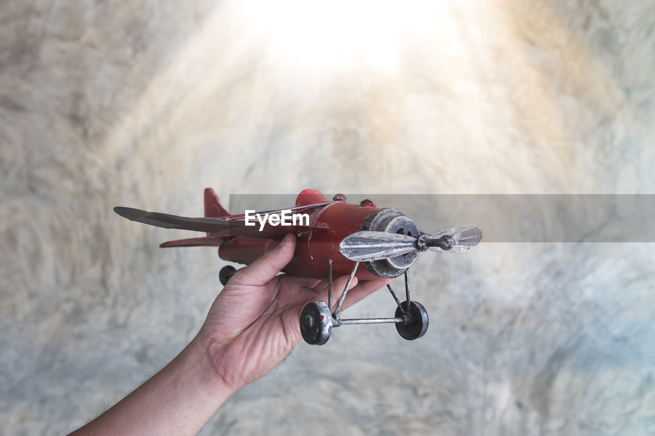 Cropped hand of woman holding toy airplane against wall