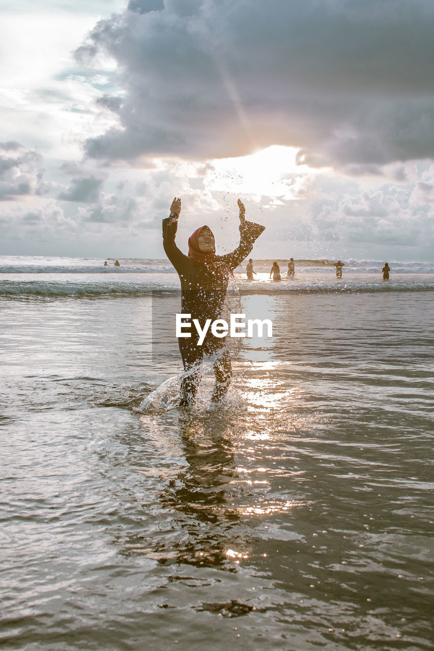 Woman splashing water in sea against sky during sunset