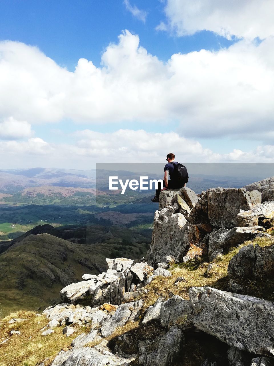 Rear view of man sitting on rock against sky