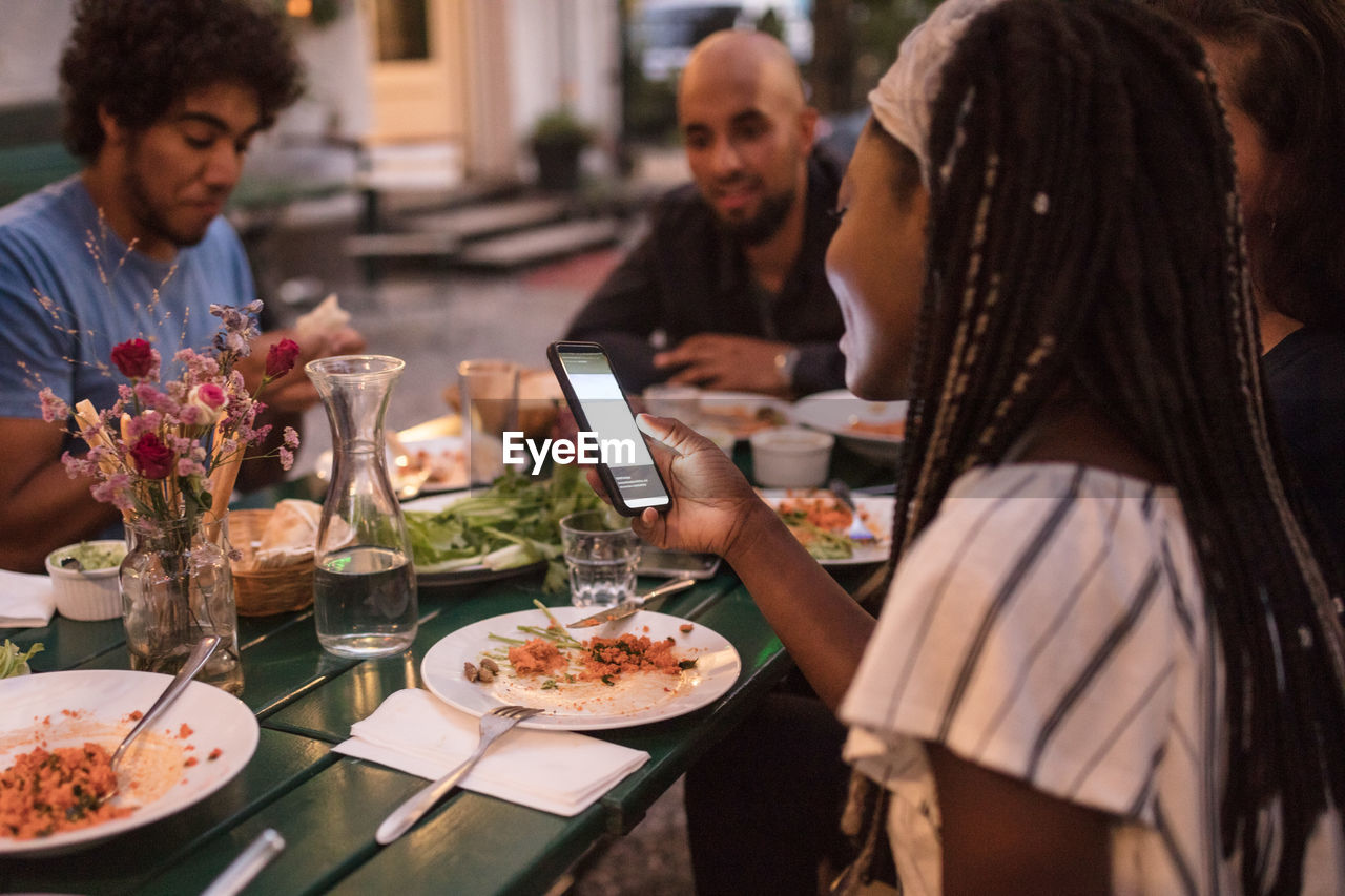 Young woman using smart phone while having dinner with friends during garden party