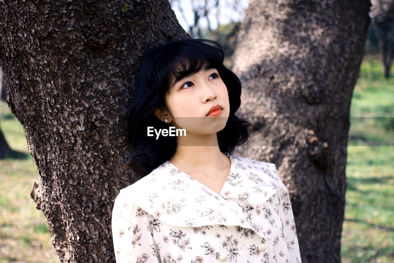 PORTRAIT OF YOUNG WOMAN STANDING BY TREE