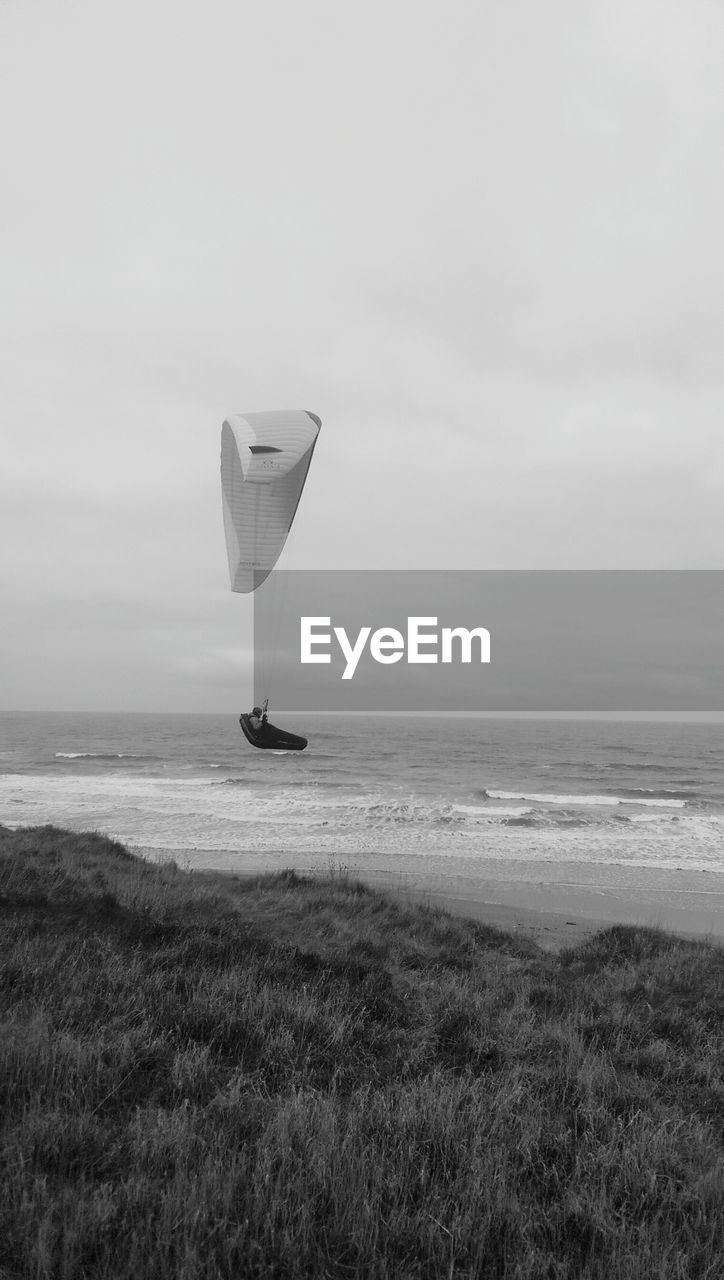 Powered hang glider over beach against sky