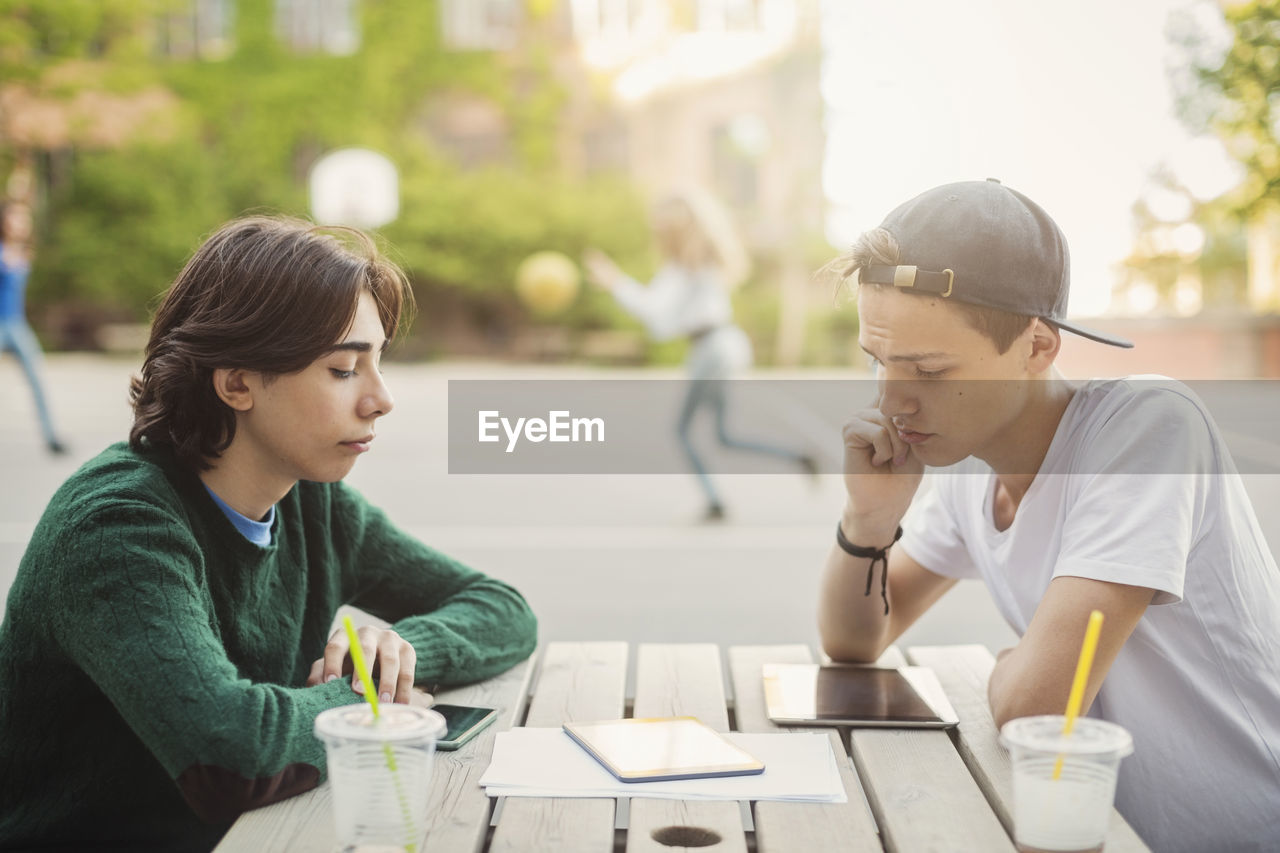 Teenagers using digital tablet at table outdoors