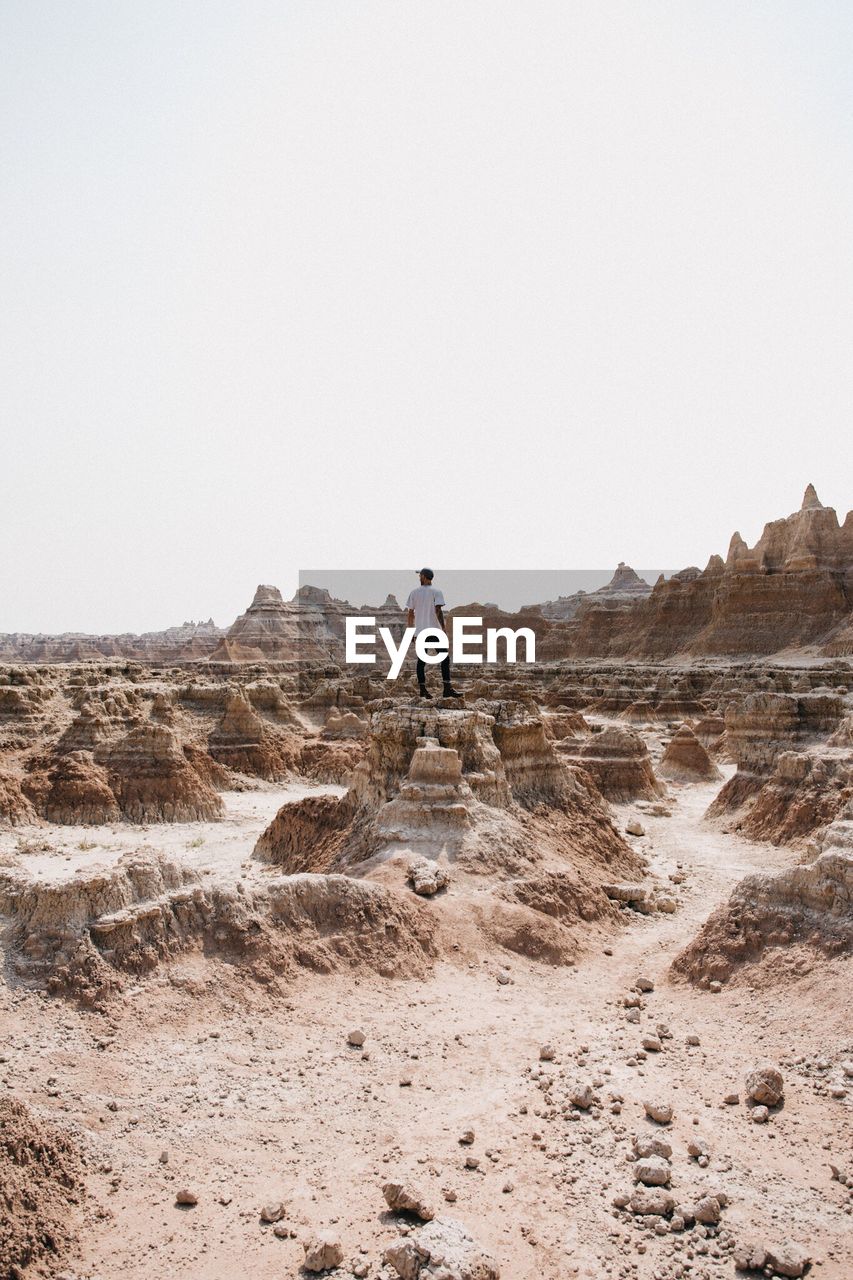 Man standing on rock in desert against clear sky